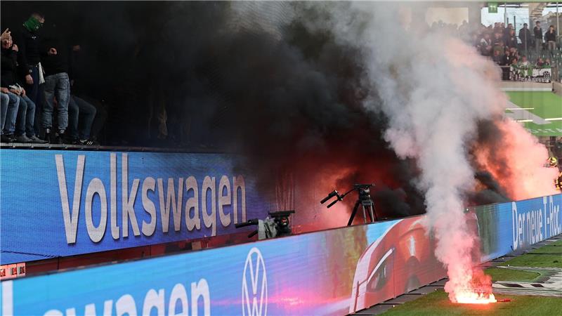  Fans von Wolfsburg werfen Leuchtfackeln auf den Platz.