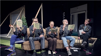 Fünf Personen sitzen auf einem Sofa auf einer Bühne und halten jeweils ein Buch oder Heft in der Hand.