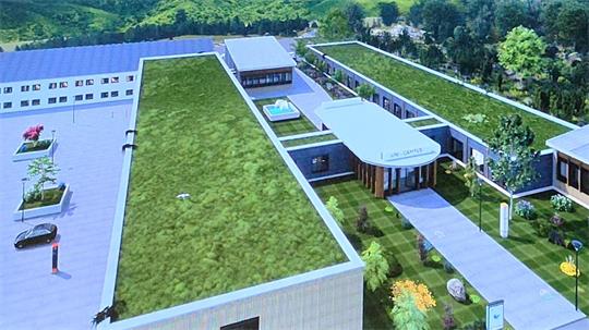 Luftaufnahme eines Gebäudekomplexes mit begrünten Flachdächern, umgeben von Bäumen und Parkplätzen