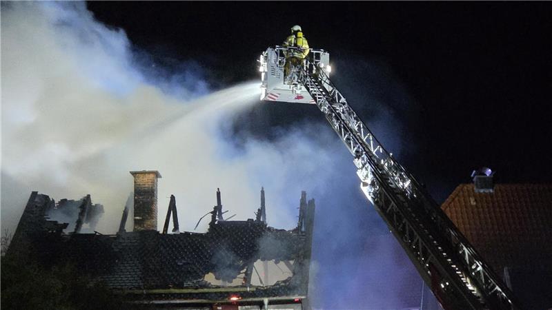 Von einer Drehleiter aus löscht ein Feuerwehrmann das brennende Dach.