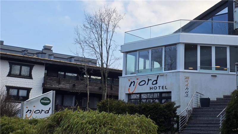 Hotelgebäude mit Glasfront und Schriftzug 'Njord HOTEL' vor blauem Himmel und Bäumen