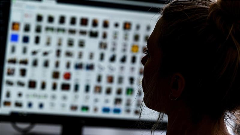 Person mit zusammengebundenem Haar vor einem Bildschirm mit vielen kleinen Symbolen oder Bildern in einem Raster.