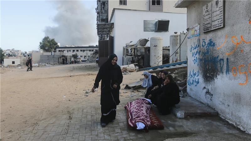 29.10.2025, Palästinensische Gebiete, Stadt Gaza: Trauernde sitzen neben der Leiche eines Palästinensers, der bei einem Angriff der israelischen Armee getötet wurde, am Shifa-Krankenhaus. 