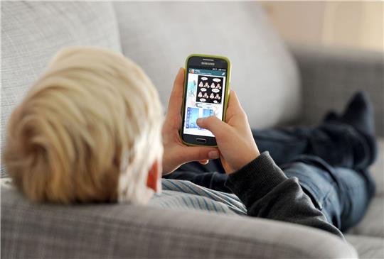 ARCHIV - Ein Kind liegt auf einem Sofa und blickt auf sein Smartphone.