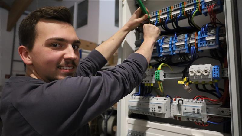 Person mit langärmligem Oberteil arbeitet an einem Schaltschrank mit mehreren Kabeln und elektrischen Bauteilen