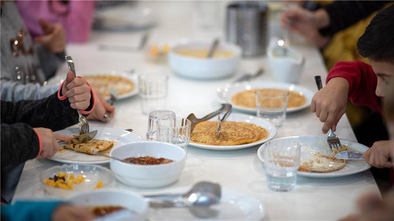 Mehrere Personen sitzen an einem Tisch und essen Pfannkuchen von weißen Tellern mit Besteck