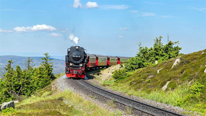 Das Foto zeigt eine Dampflok mit Personenwagen auf der Strecke oben am Brocken. 