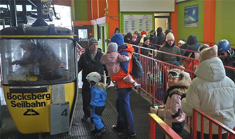 Menschen in Winterkleidung warten in einer Station auf eine gelbe Gondel der Bocksberg-Seilbahn.