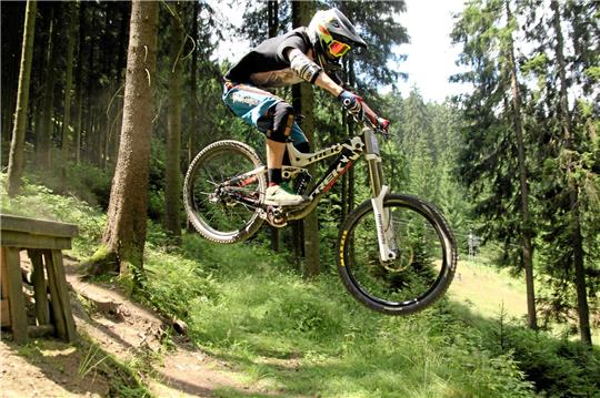Ein Mountainbiker im Racepark Schulenberg, er fährt über eine Rampe aus Holz.