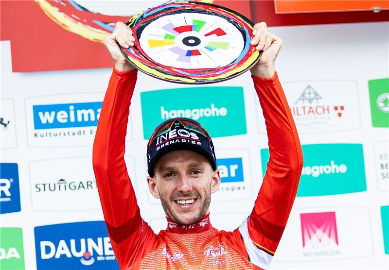 Adam Yates aus Großbritannien und dem Team INEOS Grenadiers im roten Trikot bei der Siegerehrung für den Gesamtsieg.