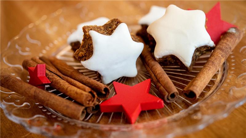 Auf dem Foto liegen mehrere Zimtsterne neben Zimtstangen und roten Holzsternen auf einem Glasteller.