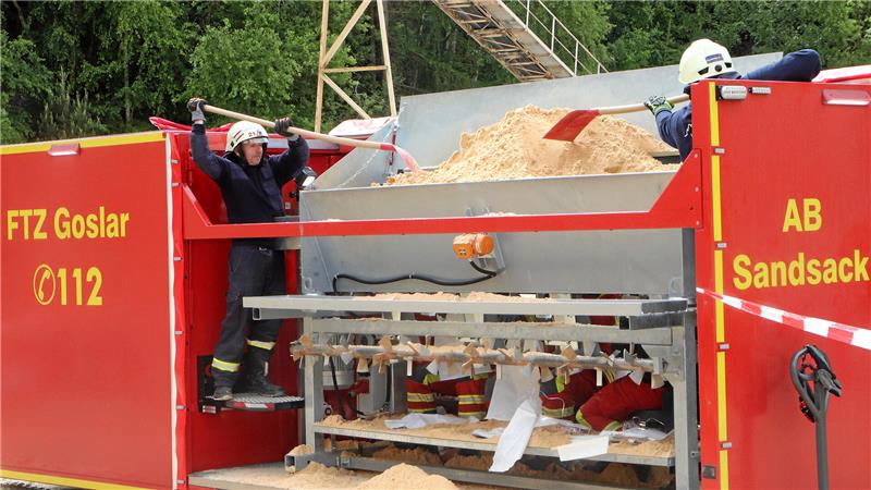 Aktive der Feuerwehr verteilen mit der Schaufel den Quarzsand im Trichter der Sandsackfüllmaschine.