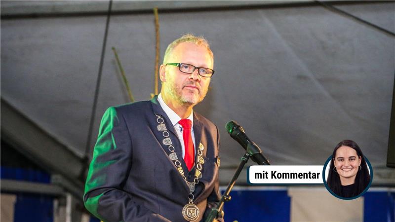 Das Bild zeigt Alexander Ehrenberg im dunklen Anzug mit roter Krawatte bei einer Rede am Mikrofon.