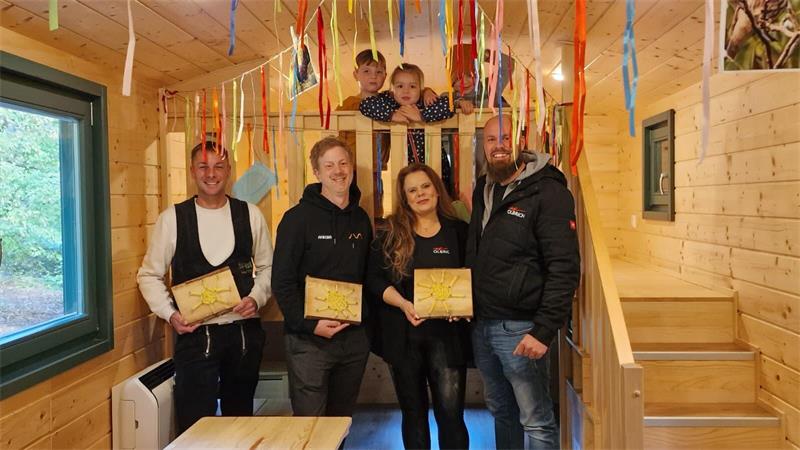 Fünf Erwachsene mit Holzplatten in einem Holzraum, zwei Kinder schauen von einer Galerie herunter.