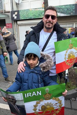 Ein Mann und sein Sohn blicken in die Kamera, in der Hand halten sie iranische Flaggen.