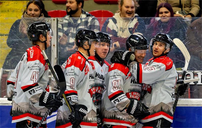 Fünf Eishockeyspieler in weißen Trikots mit roten und schwarzen Details stehen auf dem Eis und umarmen sich in einer Jubelpose