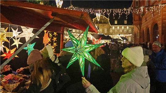 Weihnachtsmarkt bei Nacht mit beleuchteten Sternlaternen und Menschen in Winterkleidung vor Marktständen.