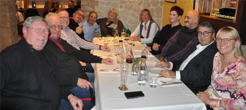 Mehrere Personen sitzen an einem langen Tisch in einem Restaurant, auf dem Gläser, Flaschen und ein Smartphone liegen.