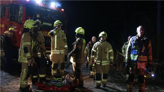 Mehrere Feuerwehrleute stehen in der Dunkelheit und in Einsatzkleidung vor einem Feuerwehrfahrzeug.