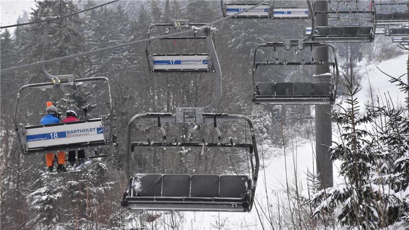 Leere und besetzte Sessellifte fahren über schneebedeckte Bäume in einem Winterwald.