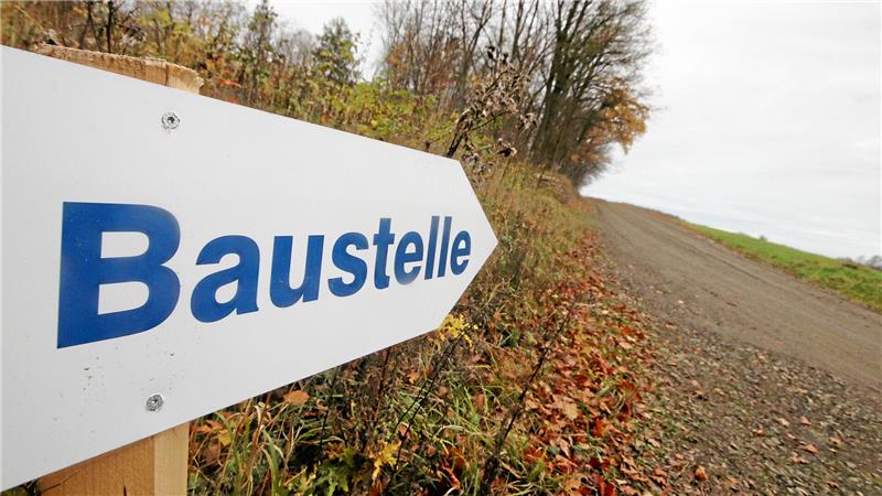 Auf dem Foto ist ein weißes Schild mit dem Wort "Baustelle" in blauer Schrift zu sehen, was an einem Waldweg. Am Hang des Salzgitterschen Höhenzugs entlang führt der Weg zur Baustelle.