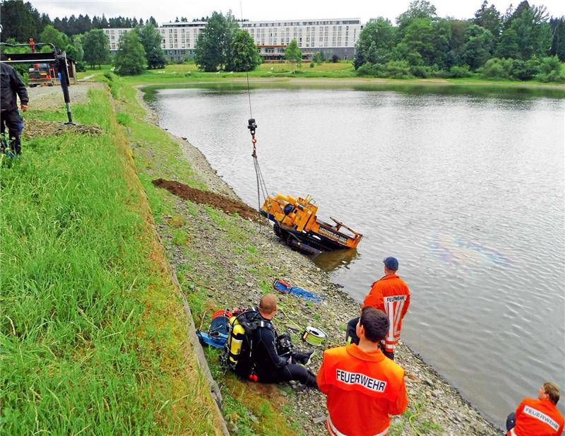 Am Kranhaken hängend, erblickt das Kettenfahrzeug wieder das Tageslicht. Es war, mit Erde beladen, auf der Dammschräge umgekippt und im Schwarzenbacher Teich versunken. Feuerwehrtaucher befestigten in rund vier Metern Tiefe die Bergeketten. Foto: Feuerwehr