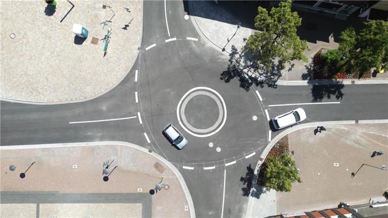 Zu sehen ist ein Kreisverkehr von ob mit Autos und Bäumen am Rand.
