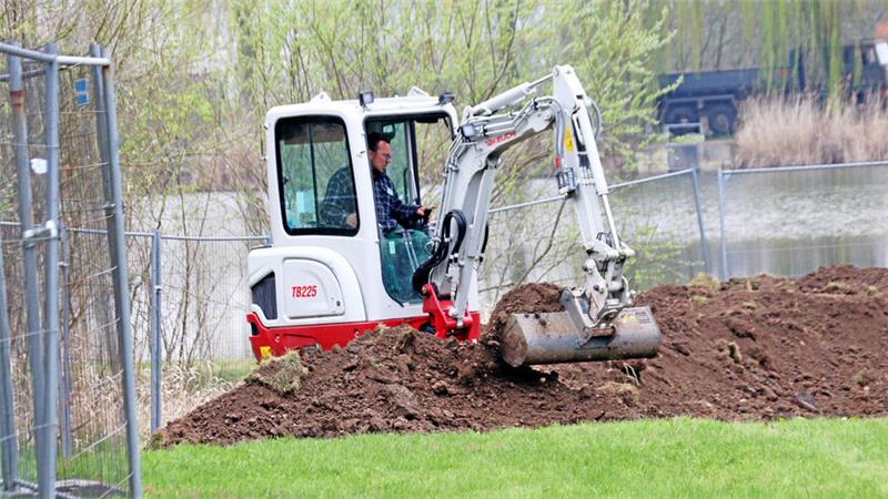 Ein Minibagger buddelt an einem Teich.