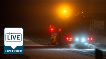 Ein Räumfahrzeug fährt in der Dunkelheit und streut Salz auf einer Straße.