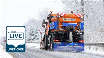 Ein Räumfahrzeug steut Streusalz auf einer winterlichen Straße.