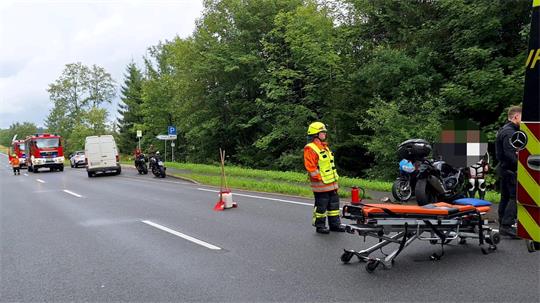 Rettungskräfte mit Trage neben einem Motorrad auf einer Straße, im Hintergrund Feuerwehrfahrzeug und weitere Fahrzeuge