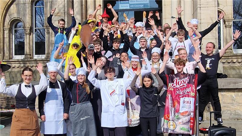 Gruppe von Menschen in verschiedenen Kostümen und Arbeitskleidung vor einem historischen Gebäude mit Rundbogenportal.