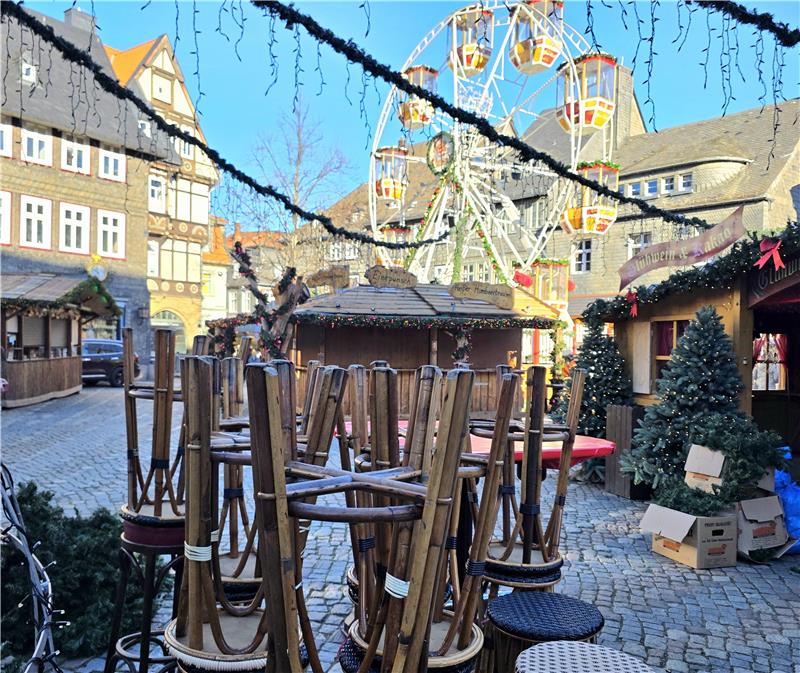 Weihnachtsmarkt mit leerem Karussell, geschmückten Tannenbäumen und aufgestapelten Stühlen auf Kopfsteinpflaster.