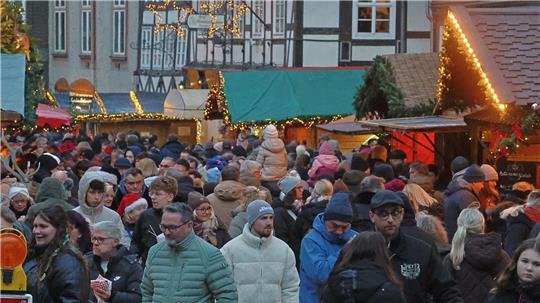 Große Menschenmenge auf einem Weihnachtsmarkt mit beleuchteten Ständen und Stern-Dekorationen in einer Altstadt.