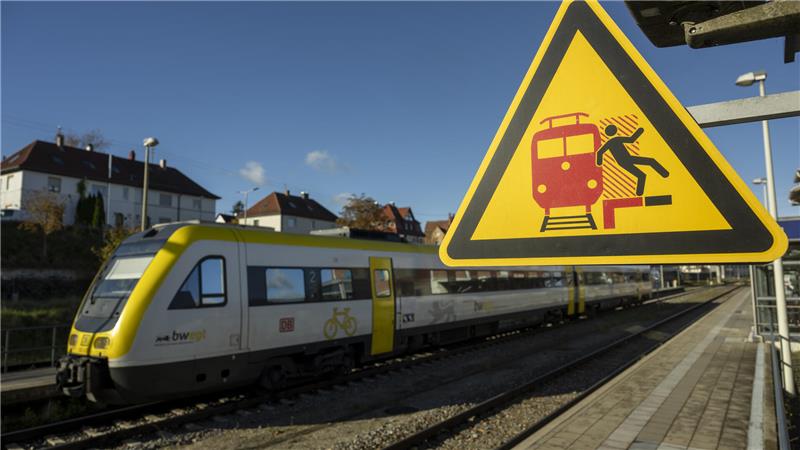 Ein Zug der DB regio fährt in einem Bahnhof unter einem Schild, das vor ein- oder durchfahrenden Zügen warnt.