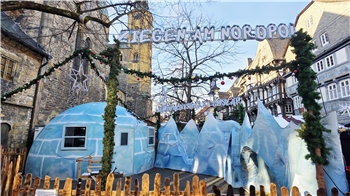 Weihnachtlich geschmückte Holzzäune umgeben ein blaues Iglu und blaue Eisskulpturen in Goslar mit Fachwerkhäusern und Kirchturm.