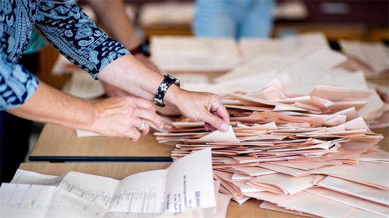 Das Foto zeigt die Hände einer Wahlhelferin, die auf einem Tisch stapelweise Stimmzettel sortiert.