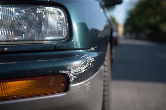 Am Stoßfänger eines geparkten Pkw sind Spuren eines Unfalls zu sehen.