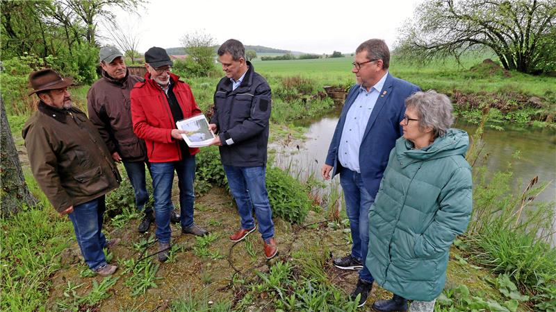 Sechs Personen stehen am Ufer eines Gewässers.