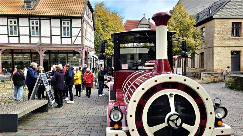 Touristischer Zug in einem historischen Ortskern mit Fachwerkhäusern und einer Gruppe von Menschen auf einem gepflasterten Platz.