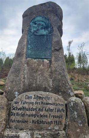 Gedenkstein mit bronzener Reliefplatte und Inschrift in einer bewaldeten Landschaft