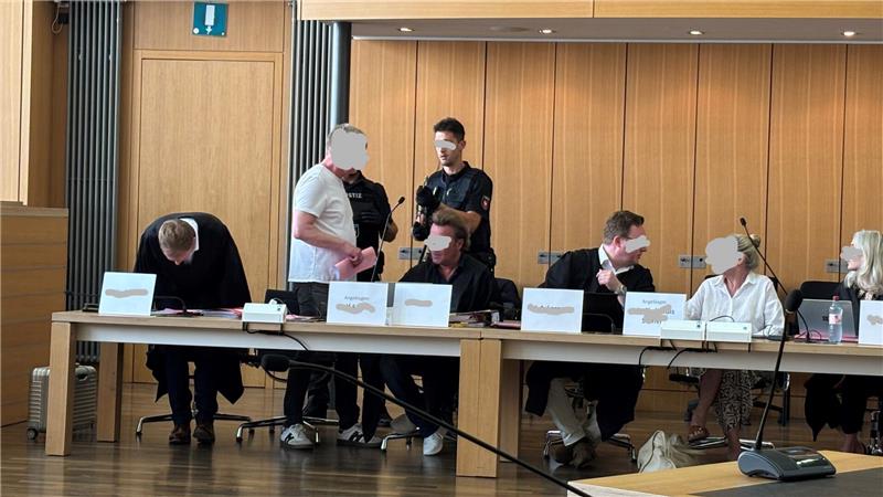 Mehrere Personen sitzen und stehen an einem langen Tisch in einem Raum mit Holzvertäfelung.