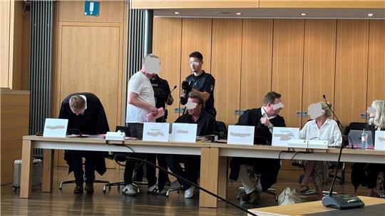 Mehrere Personen sitzen und stehen an einem langen Tisch in einem Raum mit Holzvertäfelung.