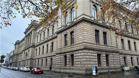 Das Braunschweiger Landgericht: ein großes historisches Gebäude mit Sandsteinfassade an einer nassen Straße, mehrere parkende Autos und Fußgänger, herbstliche Bäume mit gelben Blättern.