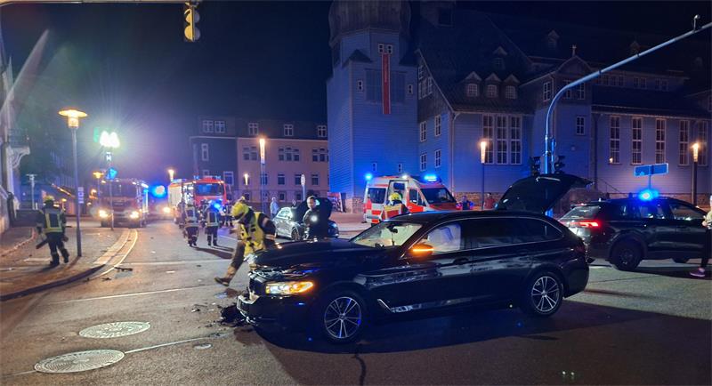 Nachtszene einer Unfallstelle mit mehreren Einsatzkräften, einem schwarzen Auto mit geöffneter Motorhaube und einem Rettungswagen.