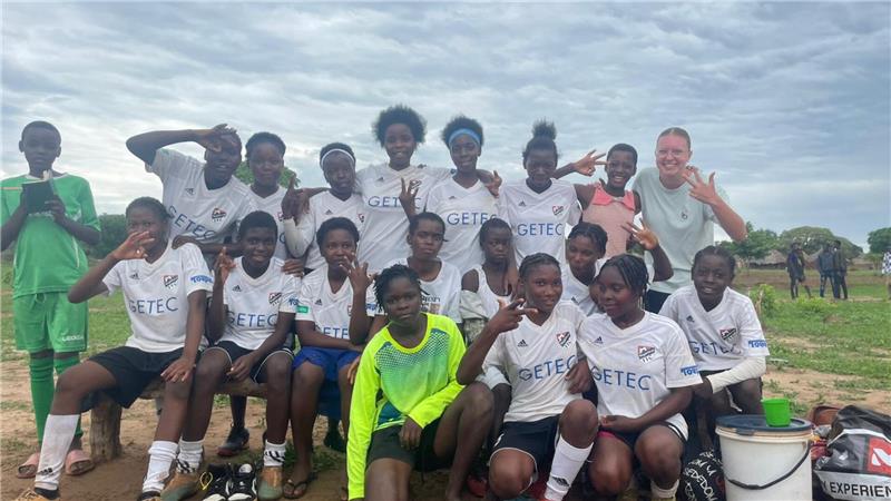 Goslarerin Amalia Saupe trainiert Mädchenteam in Afrika (Teil 2) Gruppenfoto einer Fußballmannschaft mit Spielern in weißen Trikots und einem Torwart in neongelbem Trikot auf einem Spielfeld im Freien.