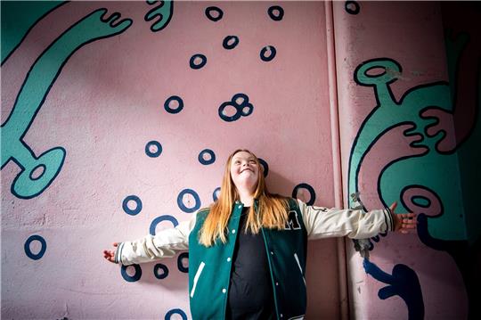 Amelie Gerdes steht an einer bunt bemalten Wand vor ihrem Tanzstudio. Die junge Bremerin mit Trisomie 21 studiert seit kurzem zusammen mit drei weiteren jungen Menschen mit Lernschwierigkeiten an der Hochschule für Künste im Sozialen (HKS) in Ottersberg. Foto: Sina Schuldt/picture alliance/dpa