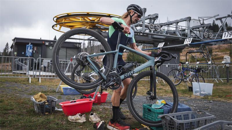 Mann mit Fahrradhelm hebt Rennrad über mehrere Kunststoffkisten im Freien