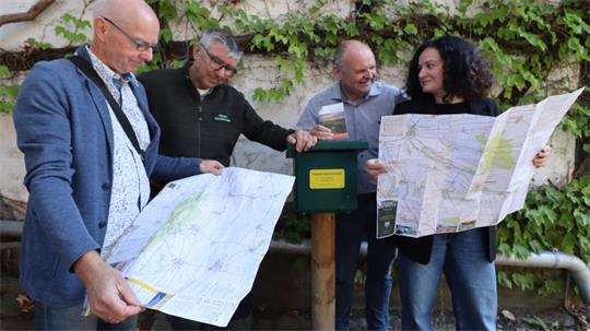 Vier Personen schauen in zwei Karten an einer Wanderstempelstelle.