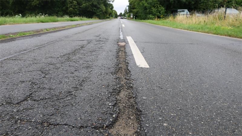 Nahaufnahme einer Straße mit deutlicher Naht zwischen altem, rissigem Asphalt und neuem, glattem Asphalt.
